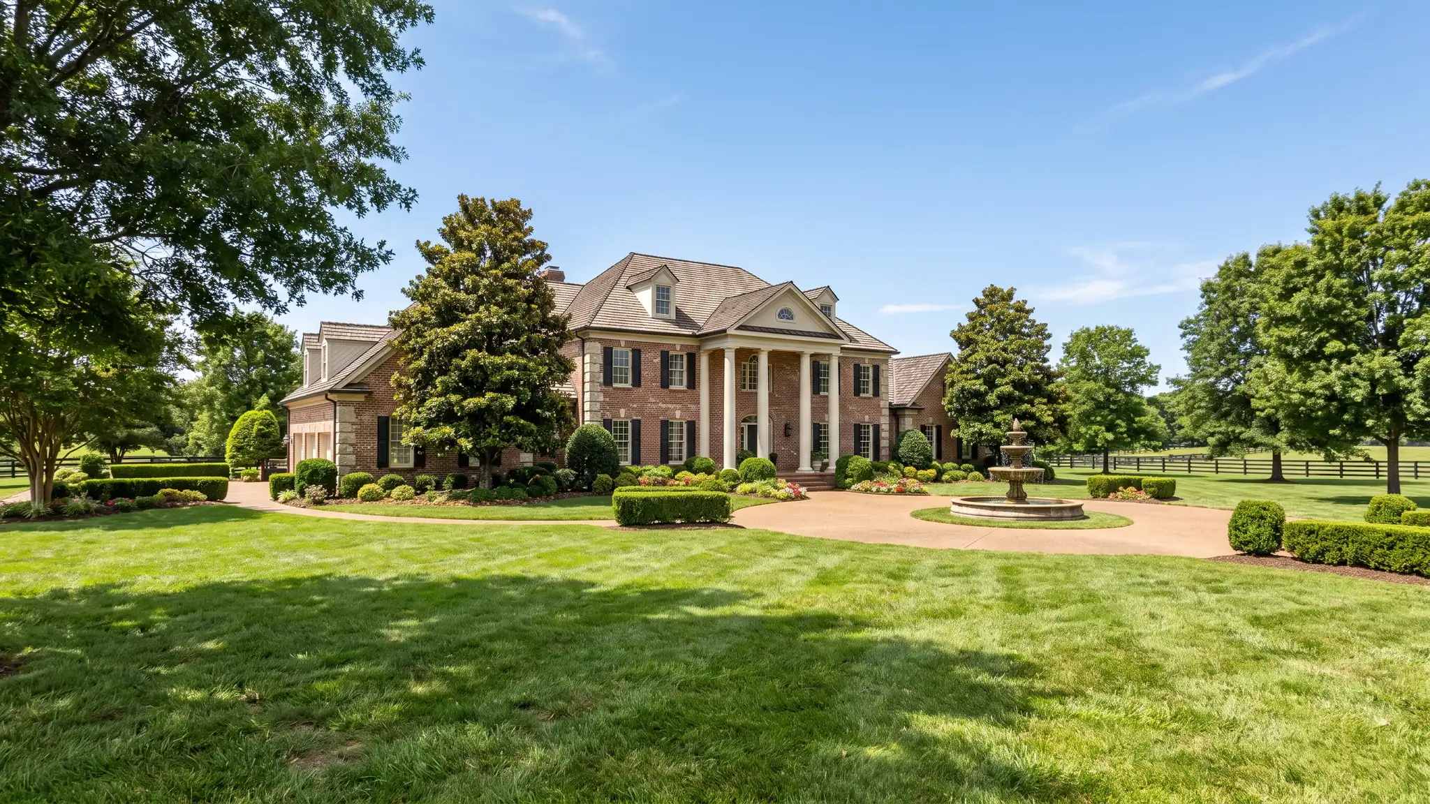A sweeping green lawn in front of a large traditional Tennessee estate home with trimmed hedges, a fountain and mature trees