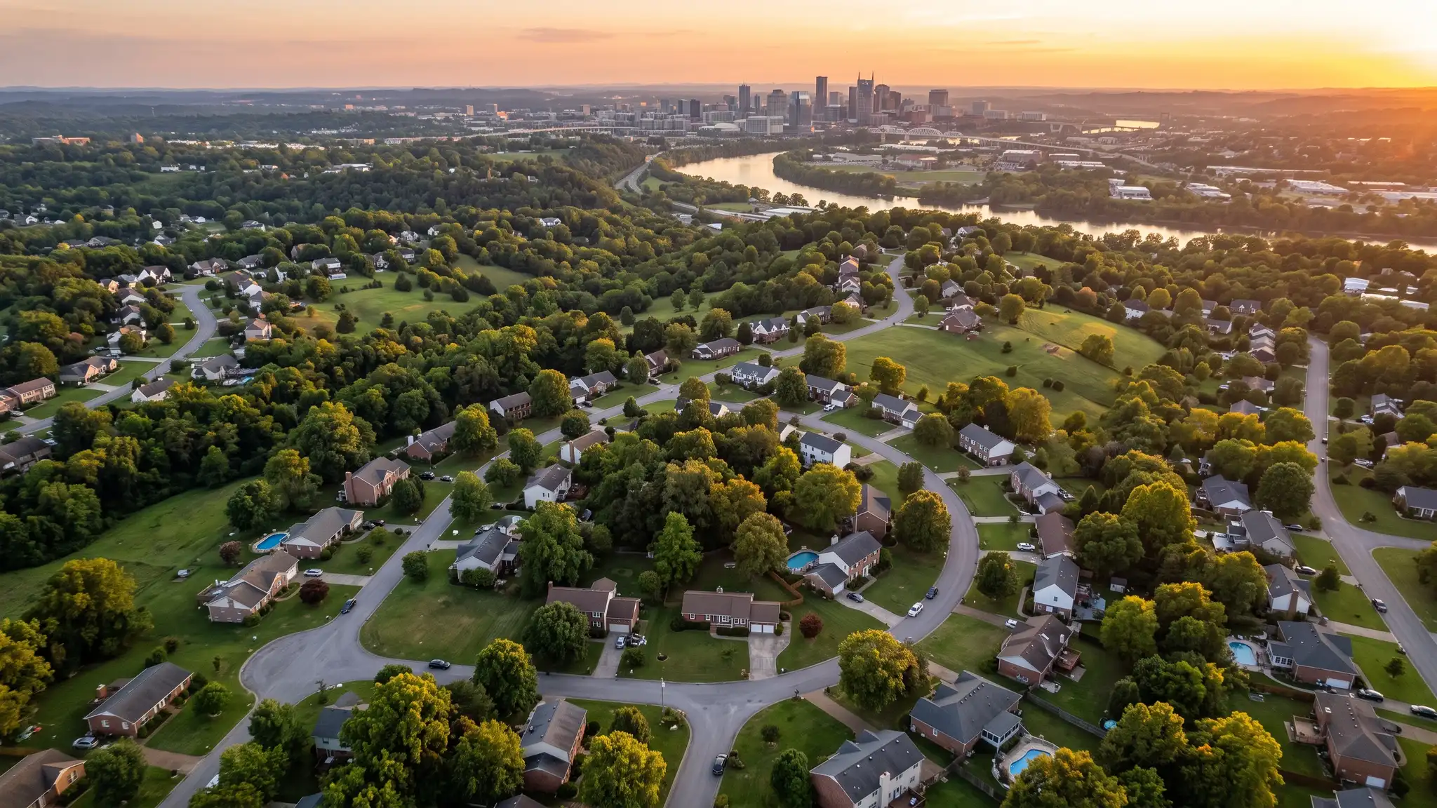 Lawn care service areas | Nashville and Middle Tennessee Aerial view of the Nashville skyline at golden hour above tree-covered suburban neighborhoods with green lawns and winding streets